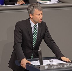 Steffen Bilger speaking at the lectern of the German Bundestag, wearing a dark suit and tie, with the blue plenary backdrop behind him