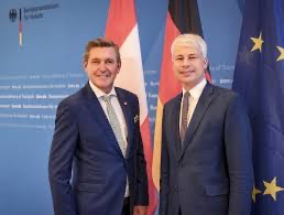 Steffen Bilger standing beside another man in front of the Austrian, German and European Union flags at the Federal Ministry for Transport