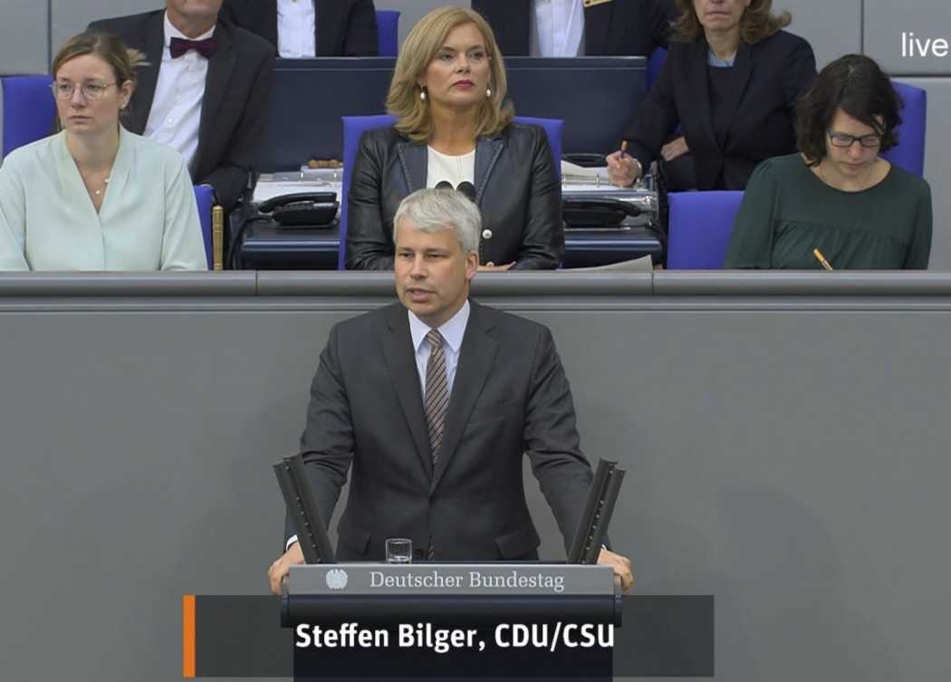 Television still of Steffen Bilger speaking at the Bundestag lectern in a dark suit, with the caption 'Steffen Bilger, CDU/CSU' and the seats of the presiding officers behind him